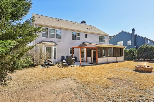 rear view of property with a fire pit, a lawn, a patio area, and a sunroom