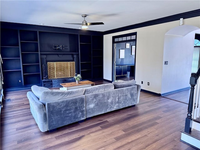 living room featuring hardwood / wood-style flooring, built in shelves, ceiling fan, and crown molding