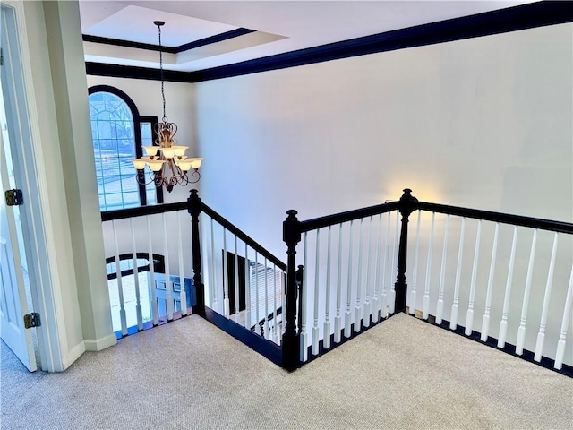 stairway with ornamental molding, a tray ceiling, and a notable chandelier