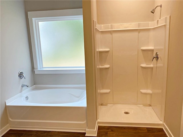 bathroom featuring baseboards, wood finished floors, a bath, and a shower