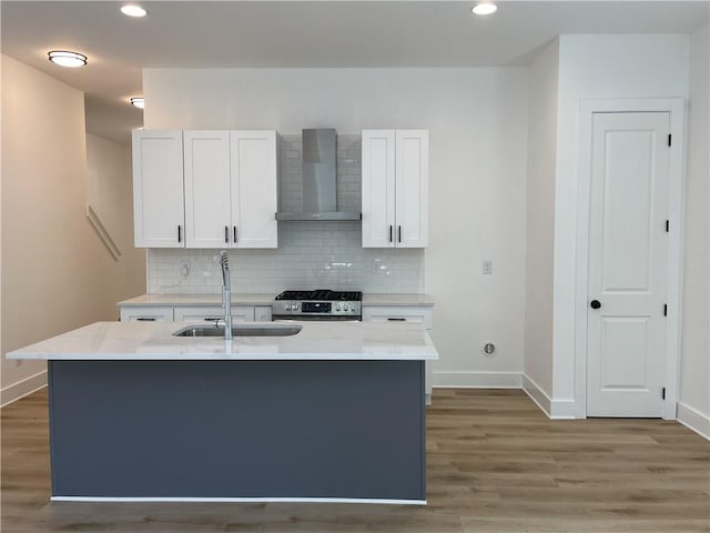 kitchen with sink, white cabinetry, wall chimney exhaust hood, stainless steel gas range oven, and a center island with sink