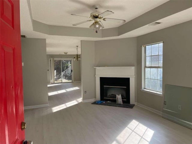 unfurnished living room featuring a tray ceiling, ceiling fan, and light hardwood / wood-style floors