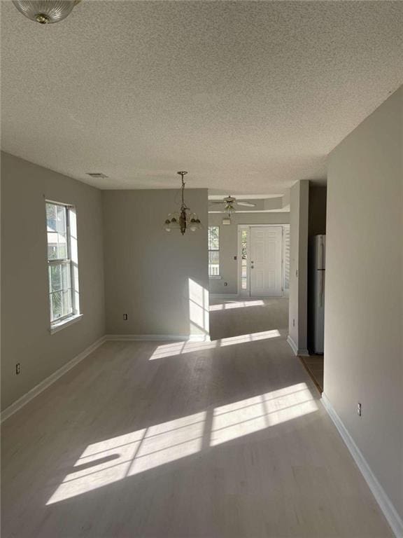 spare room featuring ceiling fan with notable chandelier, wood-type flooring, and a textured ceiling