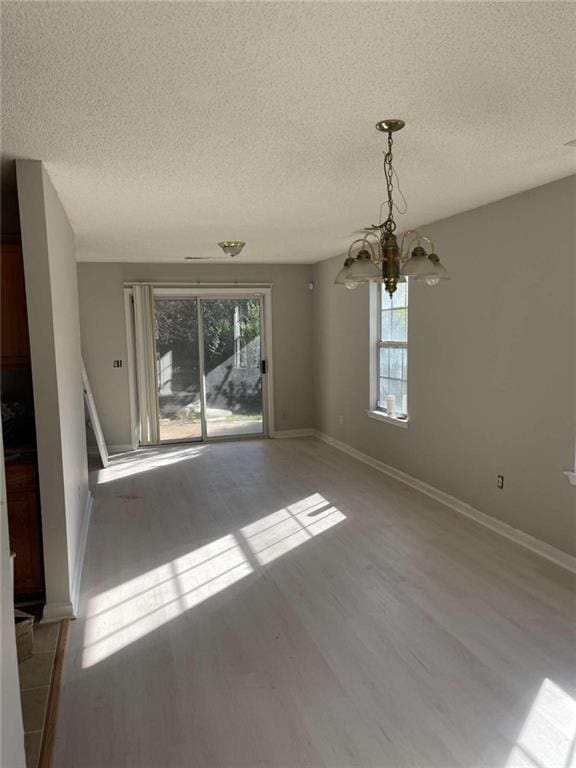 unfurnished dining area with light hardwood / wood-style floors, a textured ceiling, and a notable chandelier