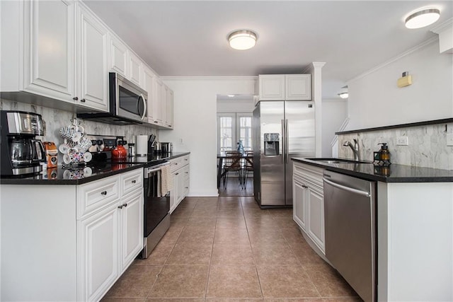 kitchen with backsplash, appliances with stainless steel finishes, dark countertops, a sink, and white cabinetry