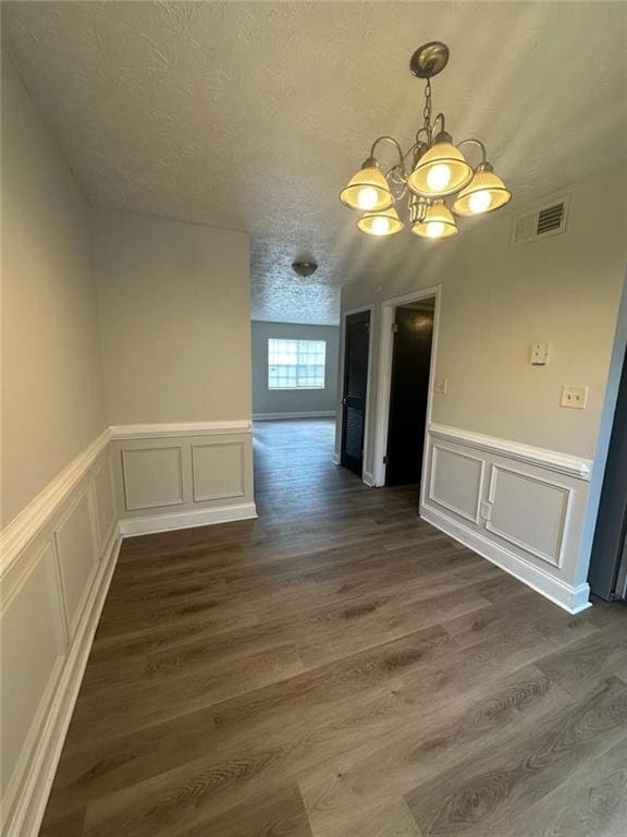 spare room featuring a textured ceiling, an inviting chandelier, and dark wood-type flooring