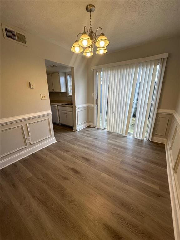 unfurnished dining area featuring dark hardwood / wood-style flooring, a chandelier, and a textured ceiling