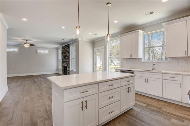 kitchen with ceiling fan, white cabinets, a fireplace, crown molding, and light hardwood / wood-style floors