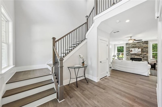 staircase with a healthy amount of sunlight, wood-type flooring, ceiling fan, and a fireplace