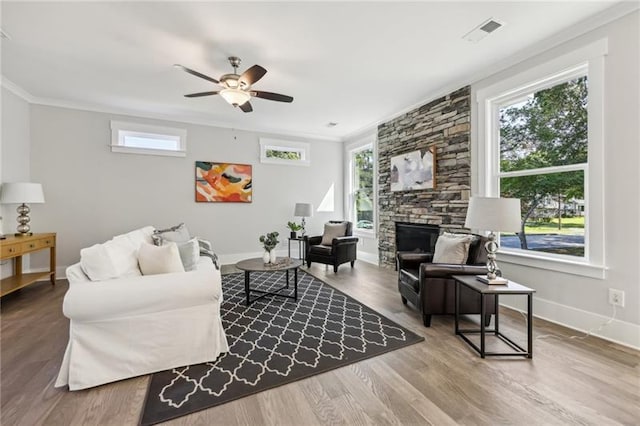 living room featuring ceiling fan, a stone fireplace, crown molding, and wood-type flooring