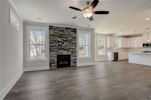 unfurnished living room with ornamental molding, ceiling fan, dark hardwood / wood-style floors, and a stone fireplace