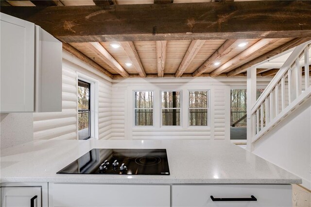 kitchen with black electric stovetop, wood ceiling, log walls, beamed ceiling, and white cabinetry