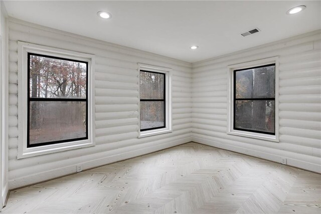 spare room featuring log walls, plenty of natural light, and light parquet floors