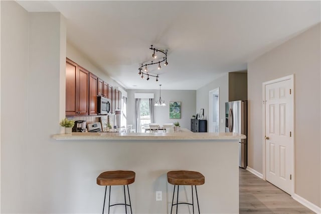 4092 Duran Ln, Auburn, GA 30011 - kitchen featuring appliances with stainless steel finishes, a peninsula, brown cabinetry, a kitchen bar, and light wood-type flooring