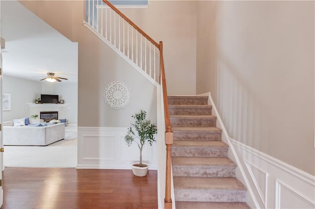 4092 Duran Ln, Auburn, GA 30011 - stairs with wood finished floors, a decorative wall, a ceiling fan, wainscoting, and a glass covered fireplace