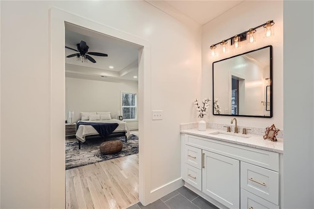 bathroom with a ceiling fan, wood finished floors, ensuite bathroom, a tray ceiling, and vanity