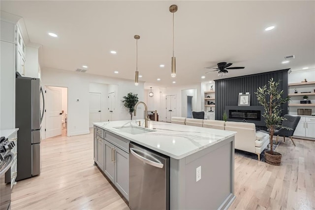 kitchen with a center island with sink, appliances with stainless steel finishes, decorative light fixtures, white cabinetry, and a sink