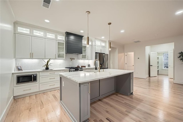 kitchen with stainless steel appliances, hanging light fixtures, glass insert cabinets, a kitchen island with sink, and white cabinetry