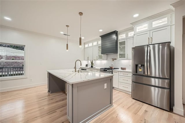 kitchen with an island with sink, light stone counters, glass insert cabinets, stainless steel appliances, and a sink