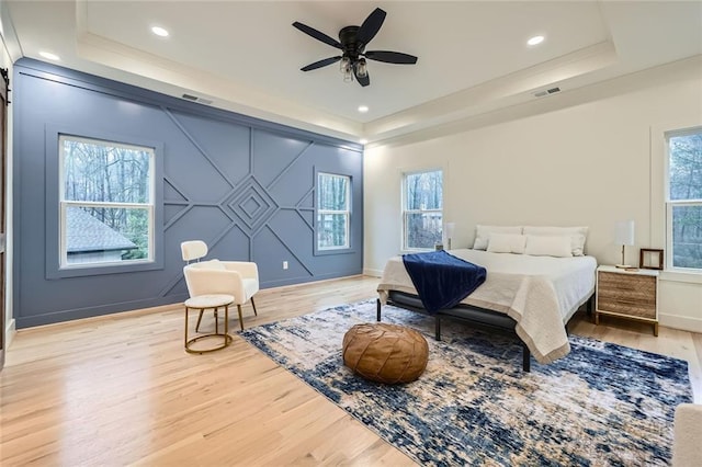 bedroom featuring an accent wall, wood finished floors, visible vents, baseboards, and a tray ceiling