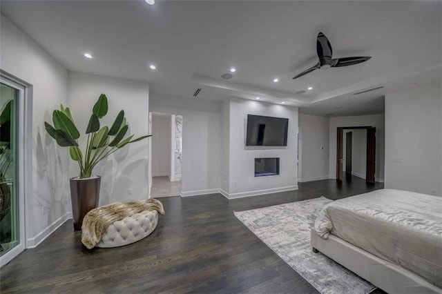 bedroom with dark hardwood / wood-style flooring, a tray ceiling, and ceiling fan