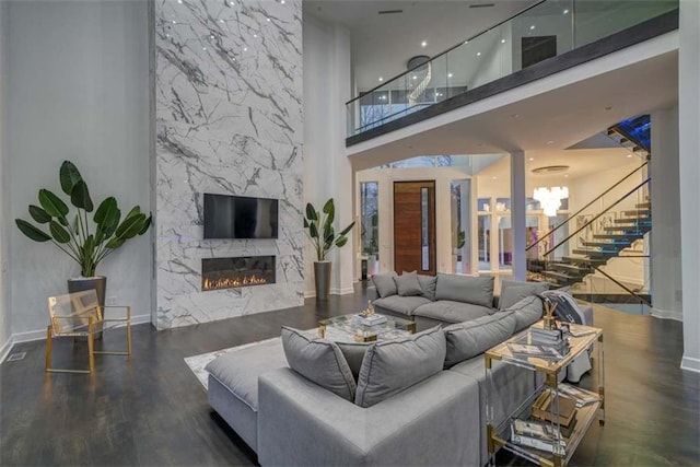 living room with a premium fireplace, dark hardwood / wood-style flooring, a towering ceiling, and an inviting chandelier