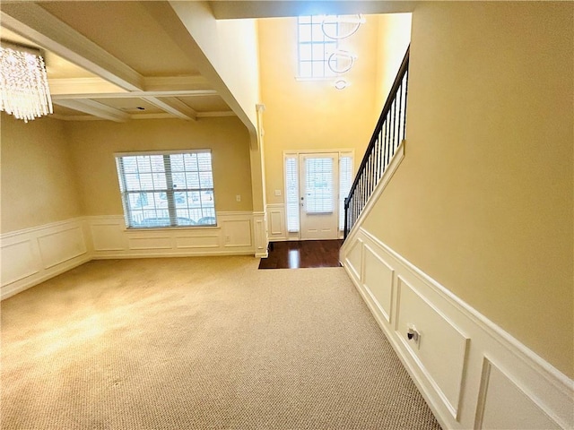 carpeted entrance foyer with a healthy amount of sunlight, coffered ceiling, a notable chandelier, and beam ceiling