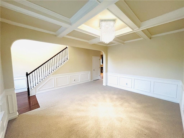 carpeted spare room featuring a notable chandelier, beamed ceiling, crown molding, and coffered ceiling