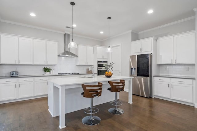 kitchen with ornamental molding, appliances with stainless steel finishes, dark wood-type flooring, a sink, and wall chimney range hood