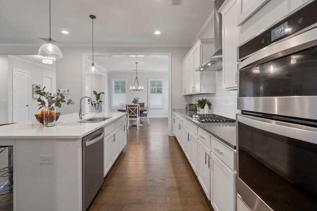 kitchen featuring appliances with stainless steel finishes, white cabinetry, a kitchen bar, decorative light fixtures, and wall chimney exhaust hood