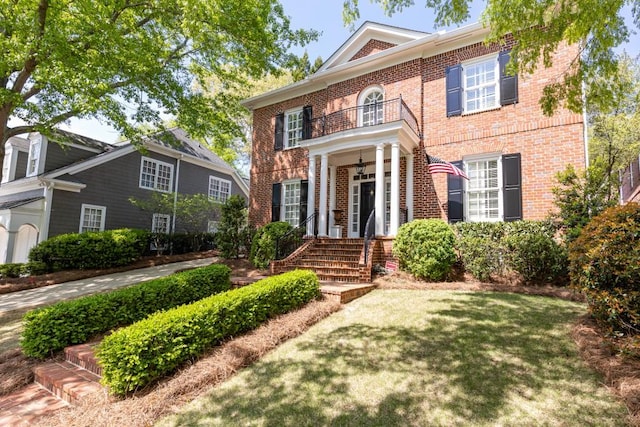 colonial house featuring a balcony, a front lawn, and brick siding