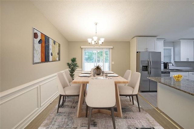 dining room with sink, hardwood / wood-style floors, a textured ceiling, and a notable chandelier