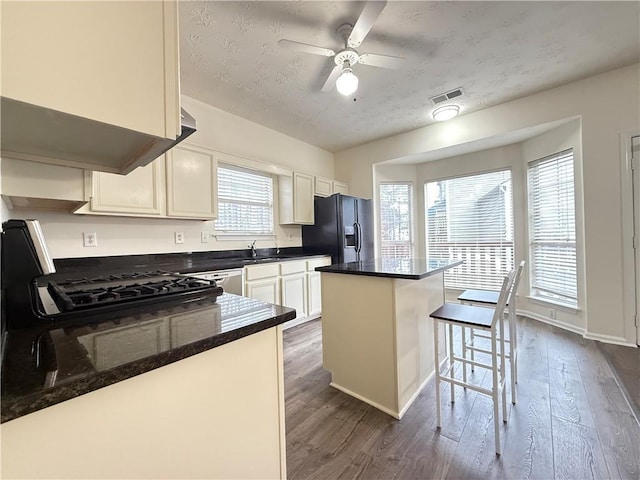 kitchen with dark wood finished floors, visible vents, black fridge with ice dispenser, and a breakfast bar