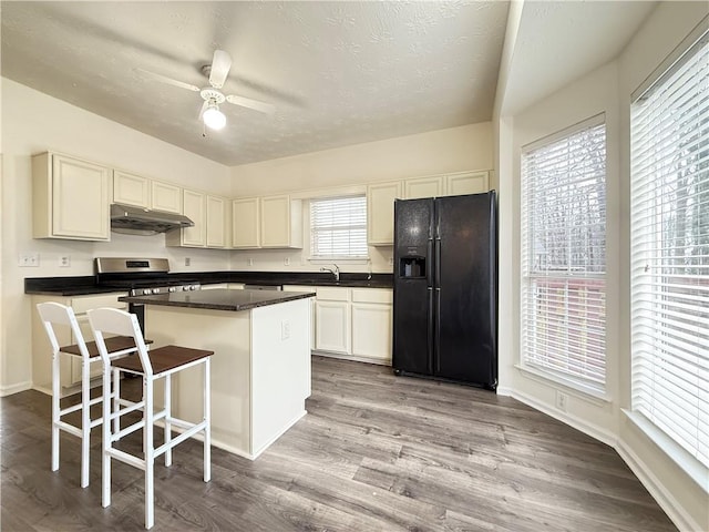 kitchen featuring a center island, under cabinet range hood, stainless steel gas stove, black fridge with ice dispenser, and a sink