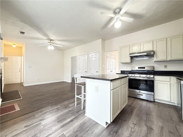 kitchen featuring dark countertops, a center island, ceiling fan, under cabinet range hood, and gas stove