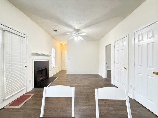 interior space featuring a fireplace with raised hearth, baseboards, dark wood finished floors, a textured ceiling, and a ceiling fan