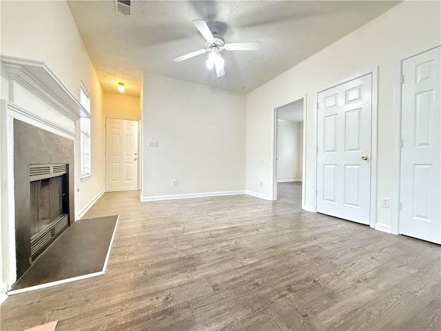 unfurnished living room featuring ceiling fan, visible vents, a fireplace with flush hearth, and wood finished floors