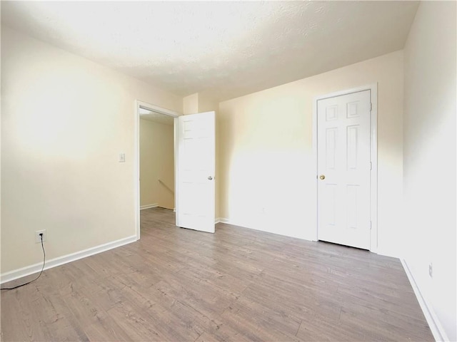 unfurnished bedroom featuring baseboards, light wood finished floors, and a textured ceiling