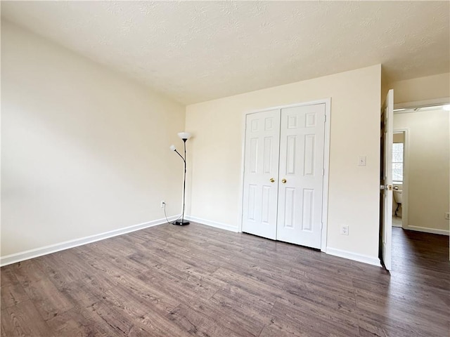 unfurnished bedroom featuring a textured ceiling, dark wood-type flooring, and baseboards