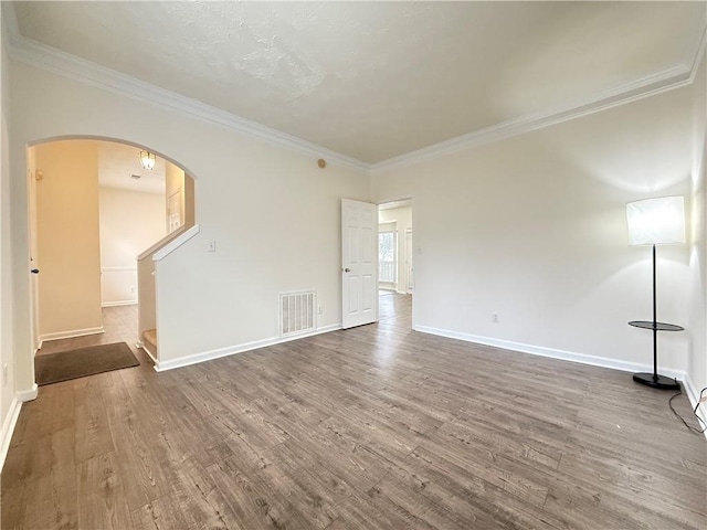 unfurnished living room with visible vents, crown molding, wood finished floors, and arched walkways