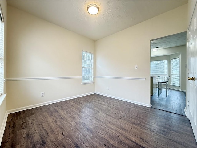 spare room featuring dark wood finished floors, a textured ceiling, and baseboards