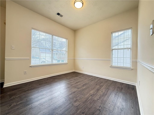 spare room with dark wood-style floors, visible vents, and baseboards