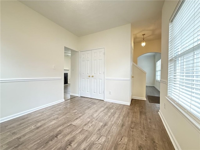 unfurnished room with baseboards, arched walkways, wood finished floors, and a fireplace