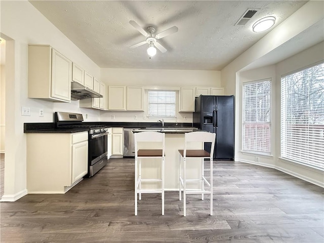 kitchen with under cabinet range hood, stainless steel appliances, a center island, and dark wood-style flooring