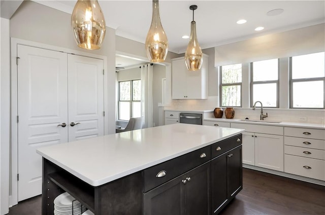 kitchen with sink, a kitchen island, stainless steel dishwasher, backsplash, and white cabinets