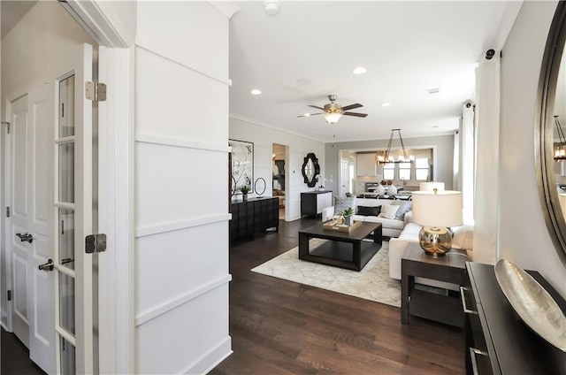 living room with ceiling fan with notable chandelier, dark hardwood / wood-style floors, and crown molding