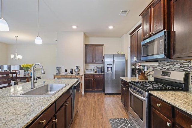 kitchen featuring wood finished floors, visible vents, a sink, stainless steel appliances, and decorative light fixtures