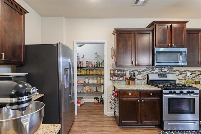 kitchen featuring visible vents, light stone counters, tasteful backsplash, dark brown cabinetry, and appliances with stainless steel finishes