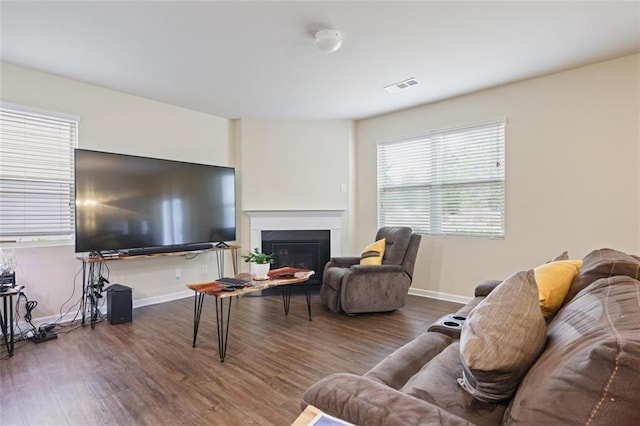 living area featuring visible vents, baseboards, a glass covered fireplace, and wood finished floors