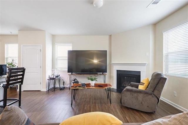 living room featuring a glass covered fireplace, visible vents, baseboards, and wood finished floors